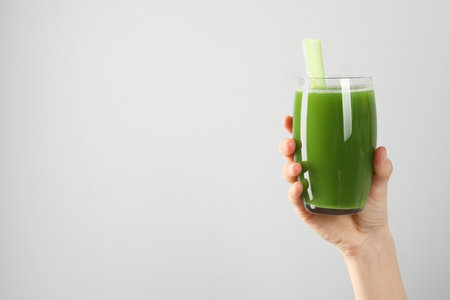 Woman holding glass of delicious celery juice on light gray background, closeup. Space for textの写真素材