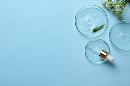 Petri dishes with samples of cosmetic oil, pipette and flowers on light blue background, flat lay. Space for textの写真素材