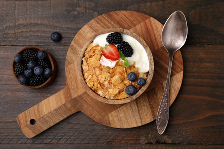 Delicious crispy cornflakes, yogurt and fresh berries served on wooden table, flat lay. Healthy...