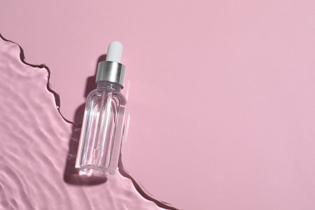 Bottle of cosmetic oil in water on pink background, top view. Space for textの写真素材