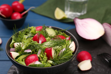 Tasty salad with radish in bowl on blue table, closeupの写真素材