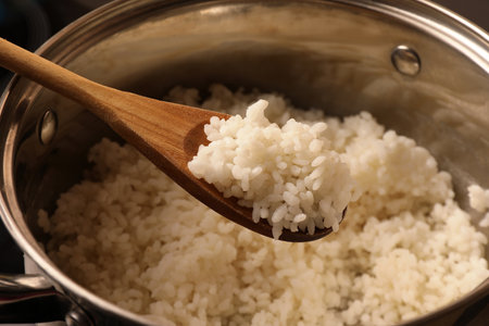 Wooden spoon with delicious rice over pot, closeupの写真素材