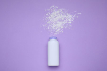 Bottle and scattered dusting powder on violet background, top view. Baby cosmetic productの写真素材