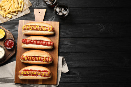 Delicious hot dogs with mustard, ketchup and potato fries on black wooden table, flat lay. Space for textの写真素材