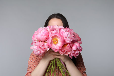 Young woman covering her face with bouquet of peonies on light gray backgroundの写真素材