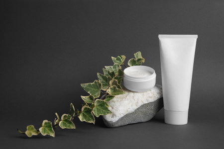 Cosmetic products, stone and ivy leaves on dark gray background