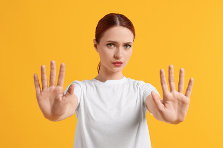 Woman showing stop gesture on yellow backgroundの写真素材