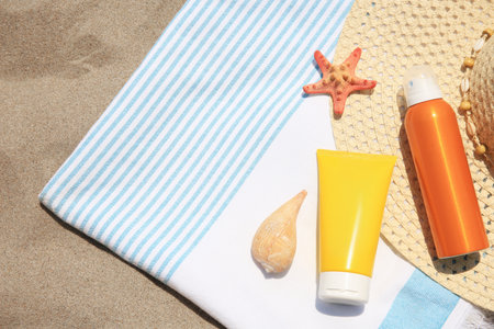 Sunscreens, starfish, seashell and beach accessories on sand, top view with space for text. Sun...