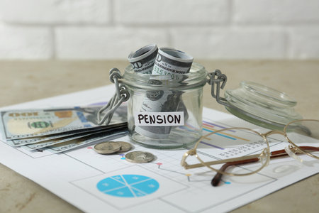 Glass jar with word Pension, money, chart and glasses on beige table, closeup