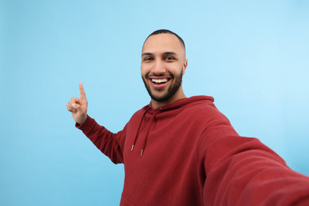 Smiling young man taking selfie on light blue backgroundの写真素材