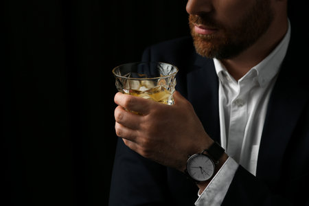 Man holding glass of whiskey with ice cubes on black background, closeup. Space for textの写真素材