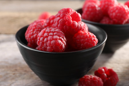 Tasty ripe raspberries in bowl on wooden table, closeup