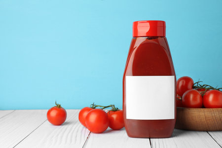 Bottle of tasty ketchup and tomatoes on white wooden table. Space for textの写真素材