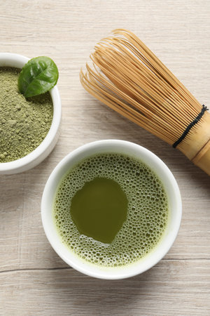Cup of fresh matcha tea, bamboo whiskey and green powder on wooden table, flat lay