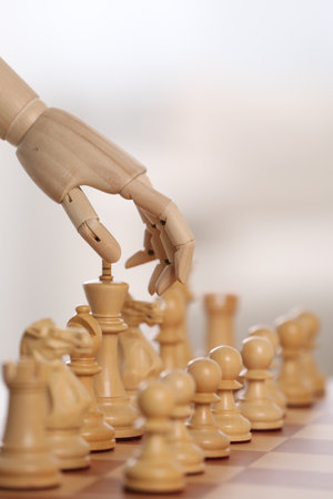 Robot moving chess piece on board against light background, closeup. Wooden hand representing artificial intelligenceの写真素材