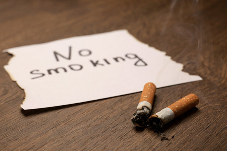 Burnt cigarettes and words No Smoking written on paper on wooden table, closeupの写真素材