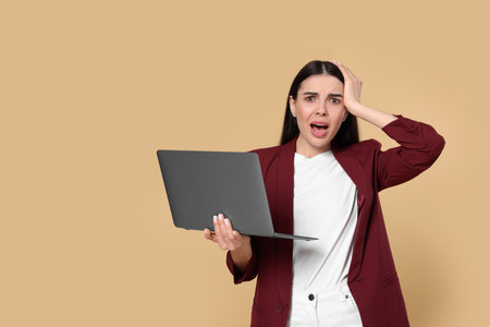 Shocked woman with laptop on beige background