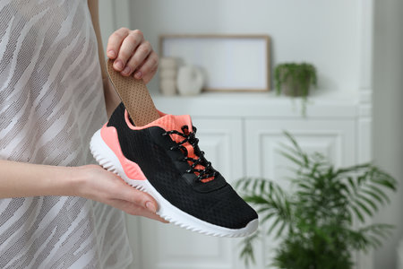 Woman putting orthopedic insole into shoe indoors, closeup. foot care
