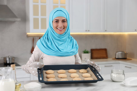Portrait of Muslim woman near tray with cookies at white table in kitchenの写真素材