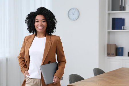 Smiling young businesswoman with laptop in modern office. Space for textの写真素材