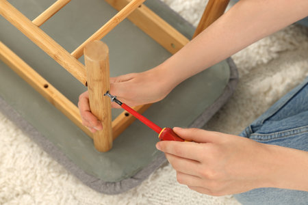 Woman with screwdriver assembling furniture on carpet, closeup