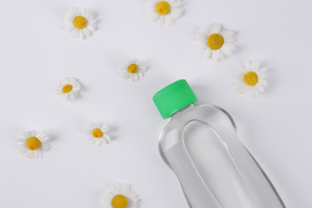 Transparent bottle with baby oil and daisies on white background, flat layの写真素材
