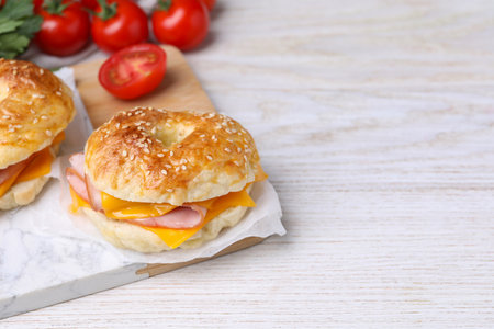 Delicious bagels with ham, cheese and products on white wooden table. Space for textの写真素材