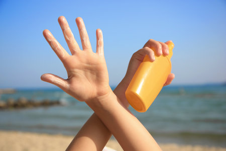 Child with bottle of sunscreen near sea, closeup. Sun protection careの写真素材