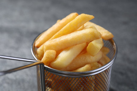 Frying basket with tasty French fries on light gray background, closeup