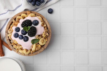 Tasty granola, yogurt and fresh berries in bowl on white tiled table, flat lay with space for text. Healthy breakfastの写真素材