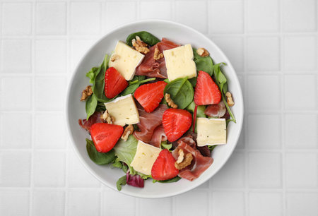 Tasty salad with brie cheese, prosciutto, strawberries and walnuts on white tiled table, top viewの写真素材