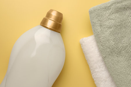 Bottle of fabric softener and towels on pale yellow background, flat layの写真素材