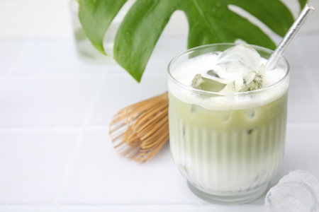 Glass of tasty iced matcha latte, bamboo whiskey and leaf on white tiled table, closeup. Space for textの写真素材