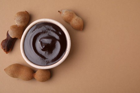 Bowl of tamarind sauce and fresh pods on light brown table, flat lay. Space for textの写真素材