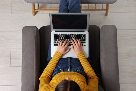 Woman working with laptop in armchair, top viewの写真素材