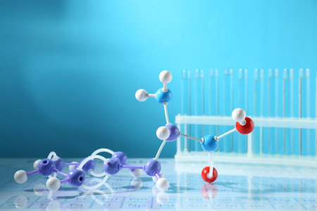 Molecular model and test tubes on periodic table against light blue background