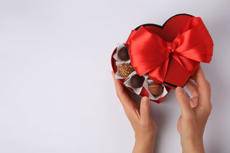 Woman with box of delicious chocolate candies on white background, top view. Space for textの写真素材