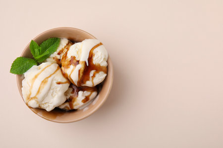 Scoops of ice cream with caramel sauce and mint leaves on beige table, top view. Space for textの写真素材