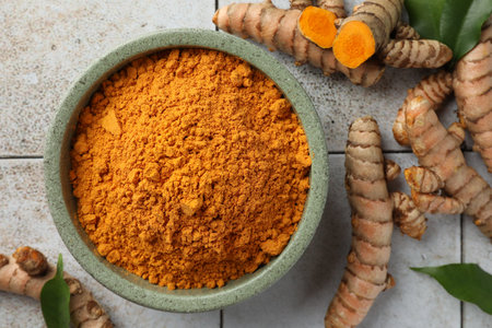 Aromatic turmeric powder, raw roots and green leaves on light tiled table, flat layの写真素材