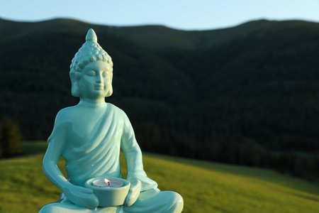 Decorative Buddha statue with burning candle in mountains, closeup. Space for textの写真素材