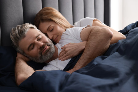 Lovely mature couple sleeping together in bed at homeの写真素材