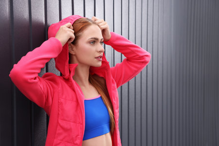 Beautiful woman in gym clothes posing near dark gray wall on street, space for textの写真素材