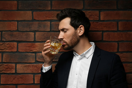 Man in suit drinking whiskey near red brick wall. Space for textの写真素材