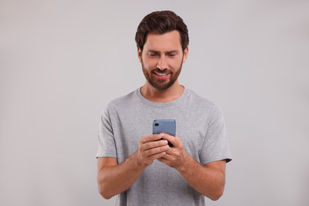 Handsome bearded man using smartphone on gray background