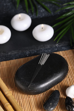 Stones with acupuncture needles and burning candles on bamboo matの写真素材