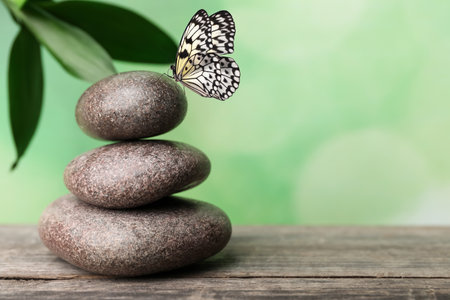 Peace and harmony. Stacked stones on wooden table and beautiful butterfly, space for text