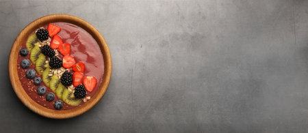 Smoothie bowl with muesli, kiwi and berries on gray table, top view. Banner design with space for textの写真素材