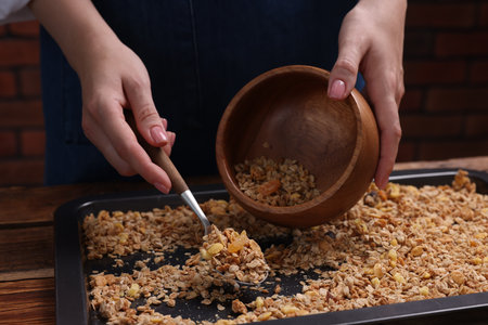 Woman putting granola from baking tray into bowl at table, closeupの写真素材