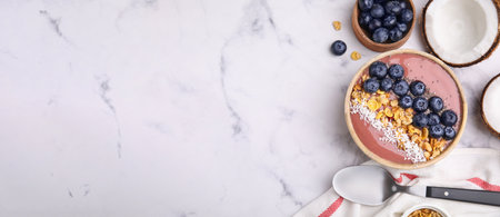Smoothie bowl with muesli, shredded coconut and blueberries on white marble table, flat lay. Banner design with space for textの写真素材
