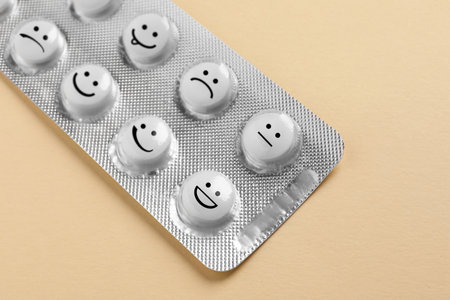 White pills with different emotional faces in blister on beige backgroundの写真素材